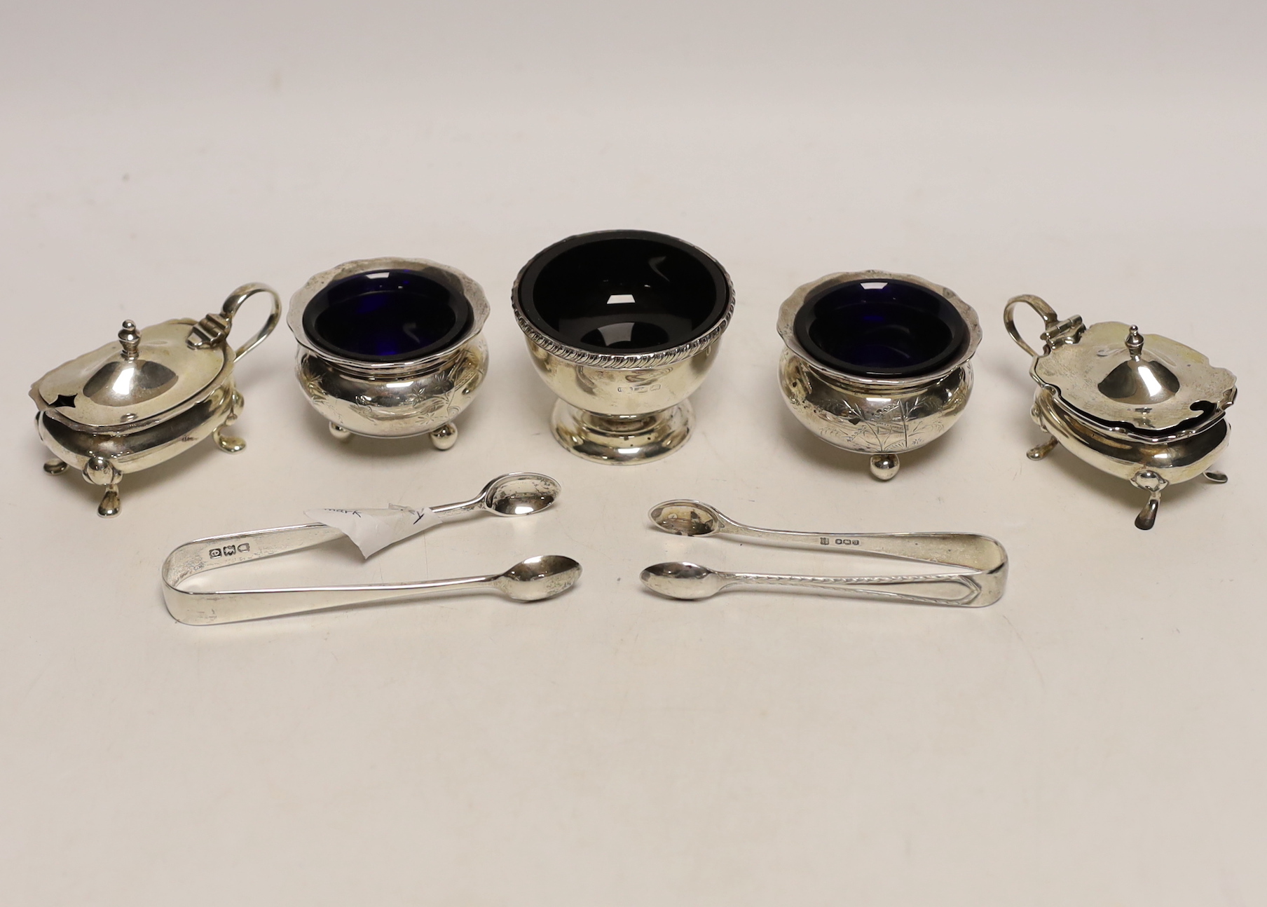 A pair of silver mustard pots, a pair of silver salts, one other silver salt, and two pairs of sugar tongs.